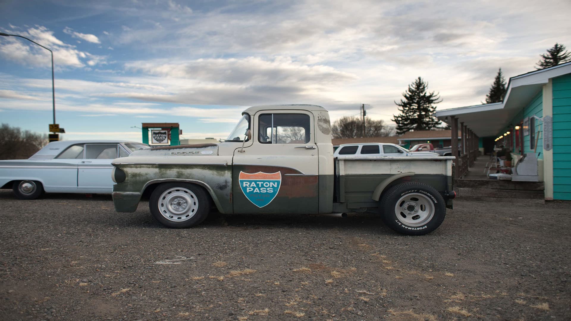 A vintage pick-up truck with Raton Pass signage is parked beside a retro diner.
