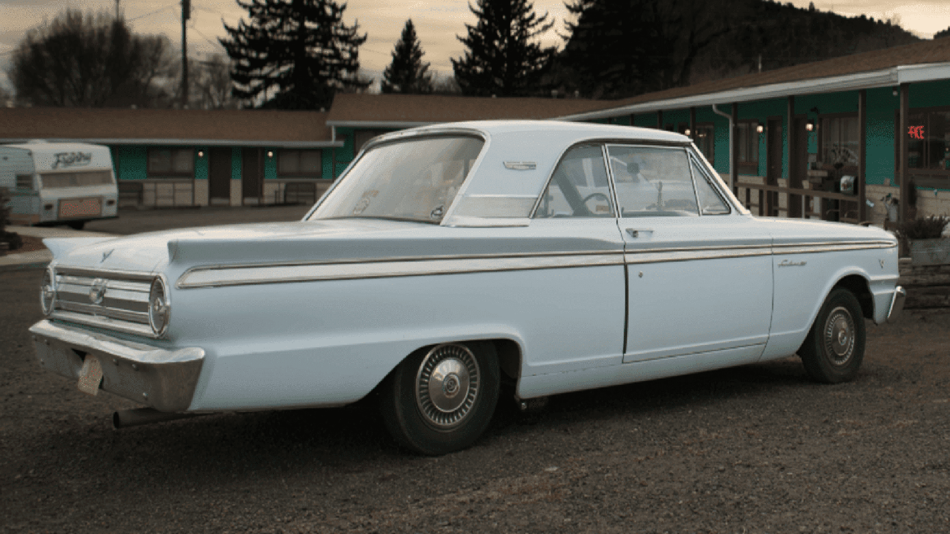 A classic light blue sedan parked outside a motel with retro-style architecture.