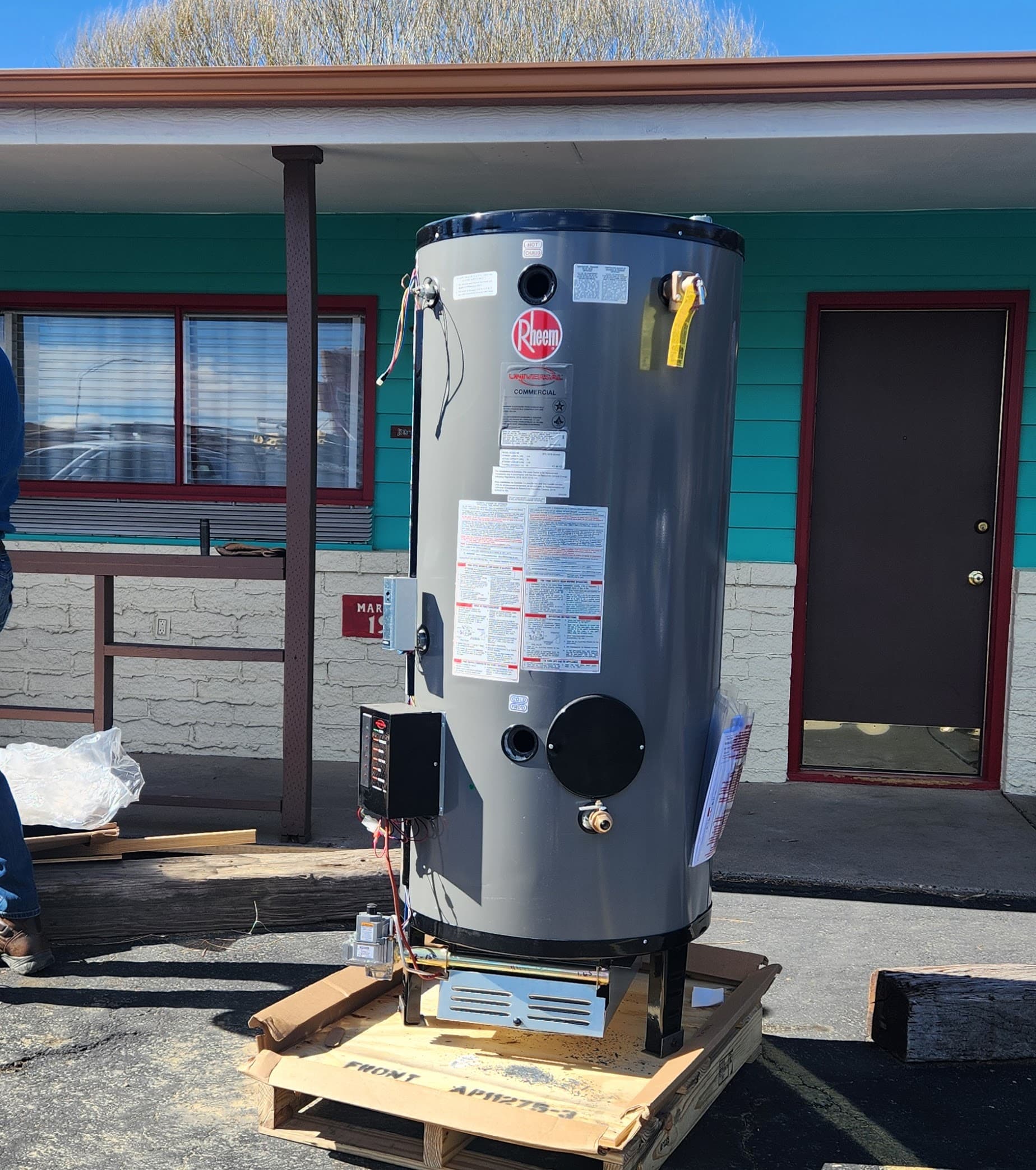 A new Rheem water heater is on a wooden pallet outside a building with a turquoise exterior and red door. A new Rheem water heater is on a wooden pallet outside a building with a turquoise exterior and red door.