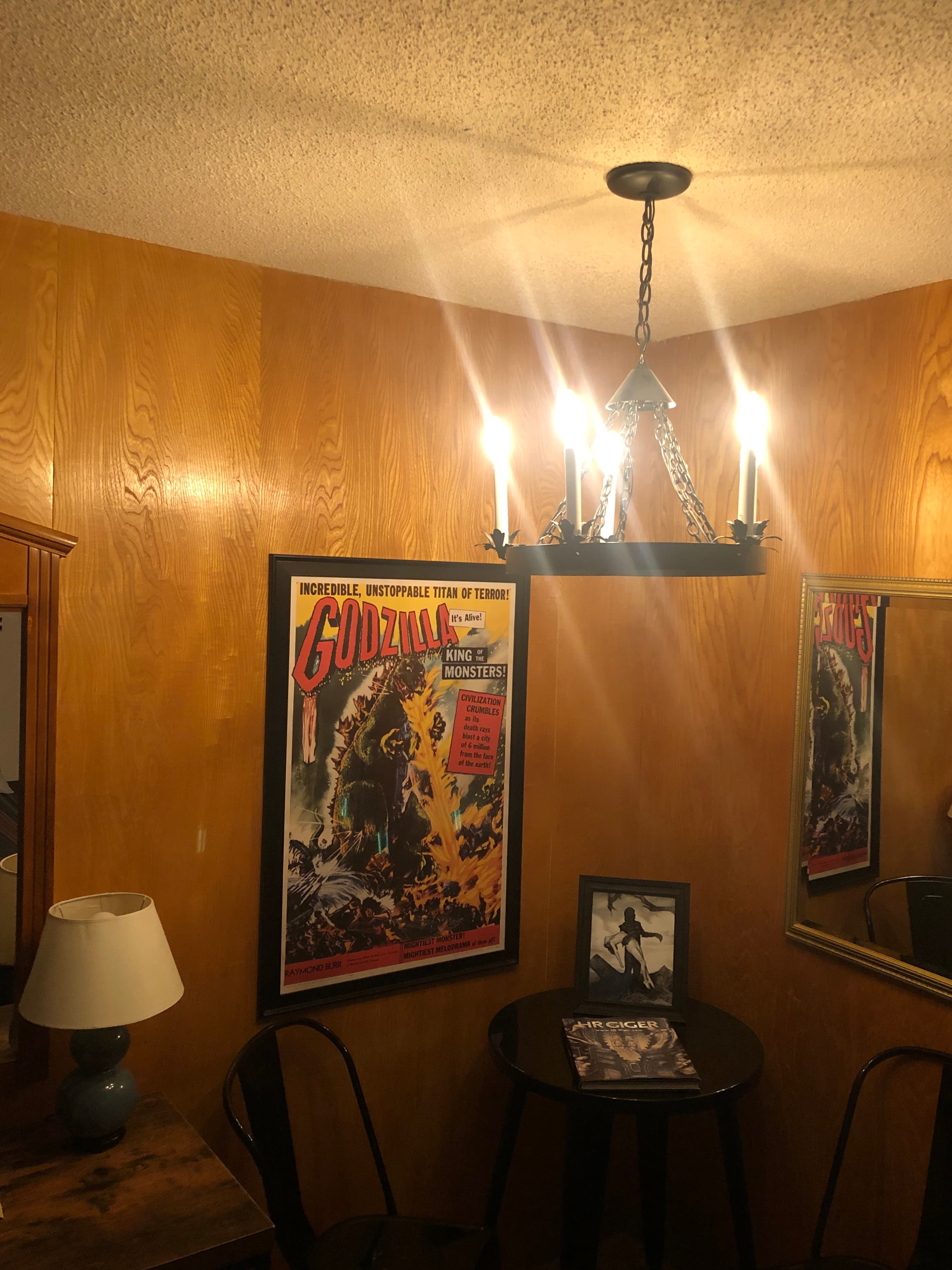 Cozy room featuring a Godzilla movie poster, a small table, a lamp, and a chandelier.