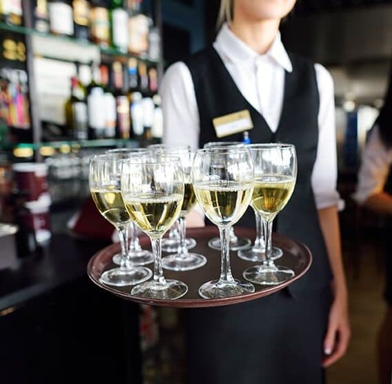 A server holds a tray of wine glasses in a bar setting.